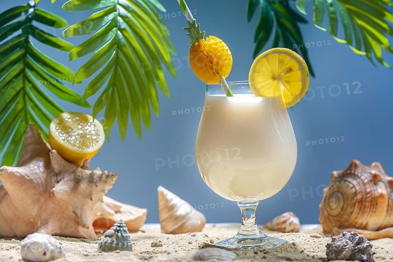 Exotic drink with lemon and straw surrounded by mussels and palm leaves