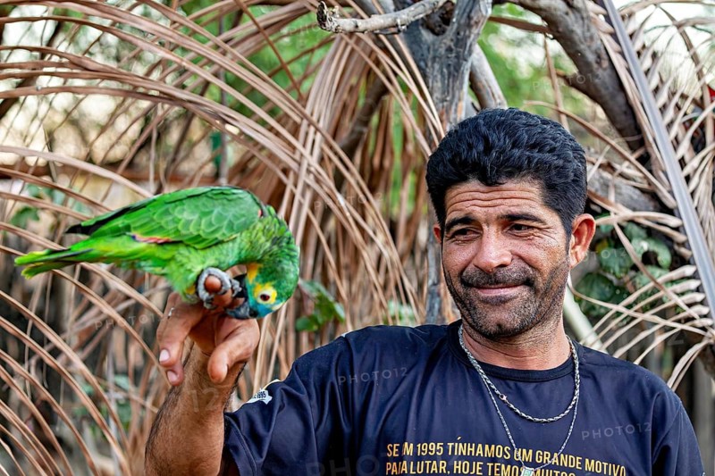 A smiling man with a parrot on his finger in a natural setting: a blue-fronted Amazon in Pernambuco, Brazil (Amazona aestiva)