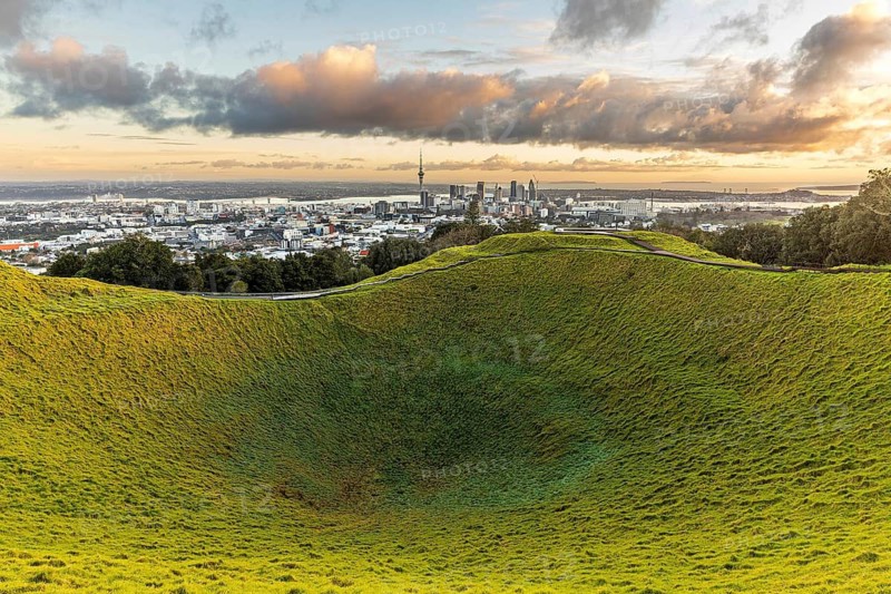 Golden morning light on the grassy volcanic crater of Mount Eden with the Auckland skyline behind, New Zealand, Auckland