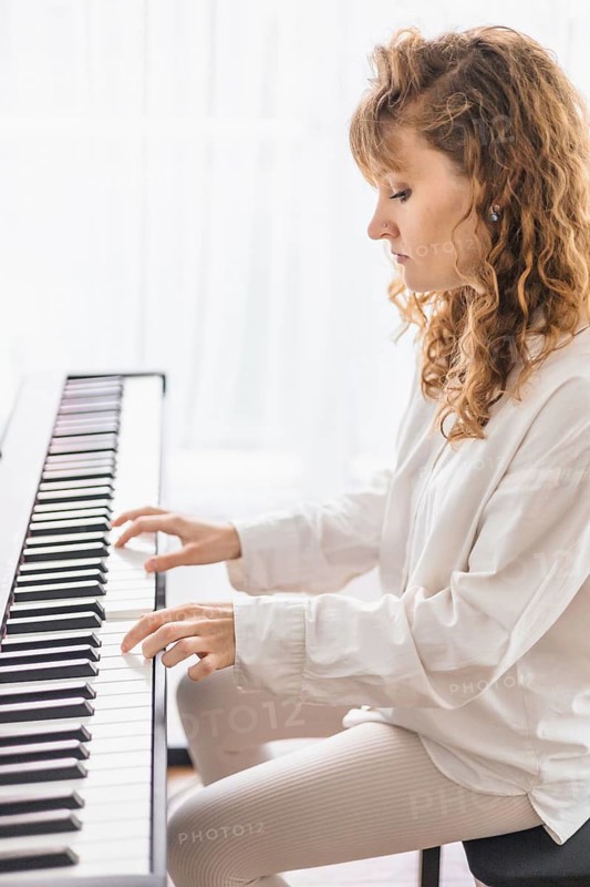 A woman intently plays the piano, bathed in soft natural light