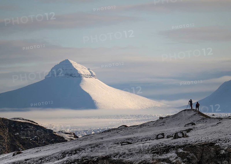 Two people, including a photographer with a stand in front of one of the three mountains Tee Kroner, Kongsfjord or Kongsfjorden, Spitsbergen archipelago, Svalbard, Norway