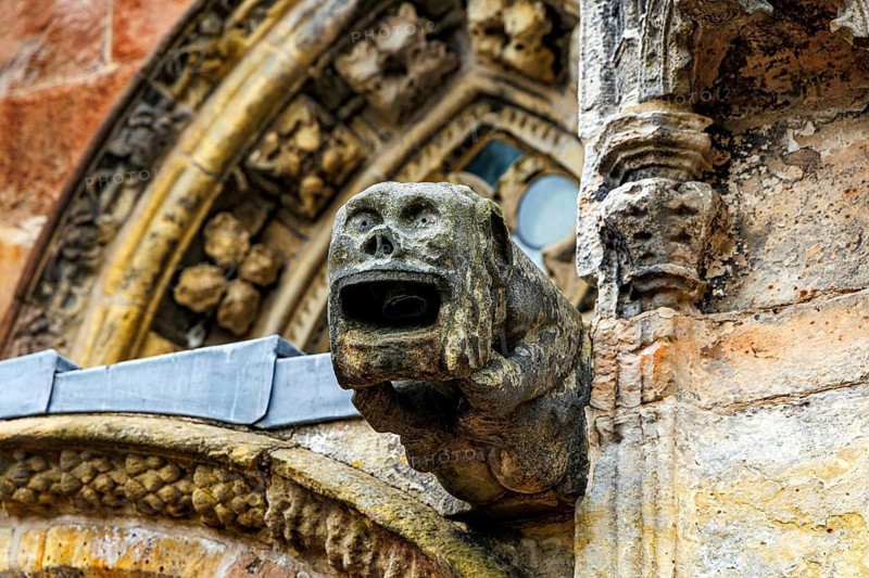 A weathered grotesque gargoyle projects from the carved stonework of 15th century Rosslyn Chapel, Roslin, Midlothian, Scotland, United Kingdom