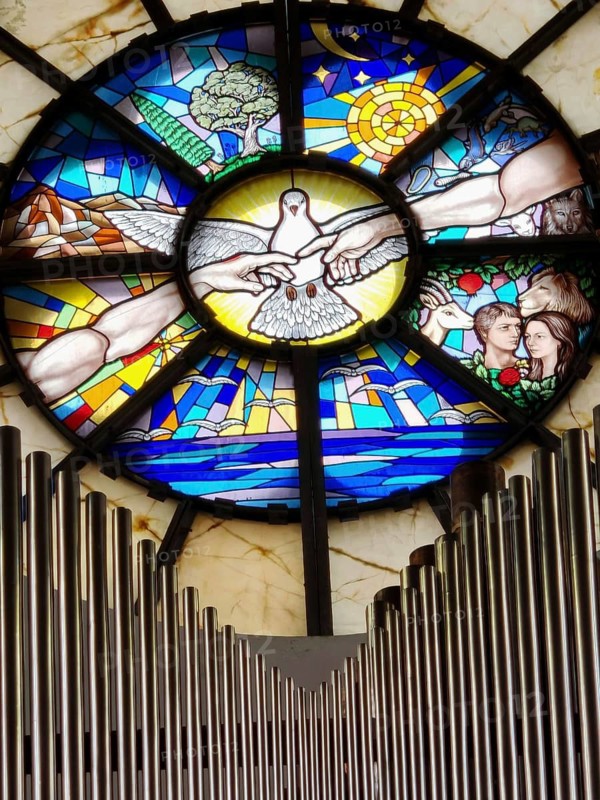 Artistic church window with a dove surrounded by colorful stained glass depictions of organ pipes, Pristina, Kosovo
