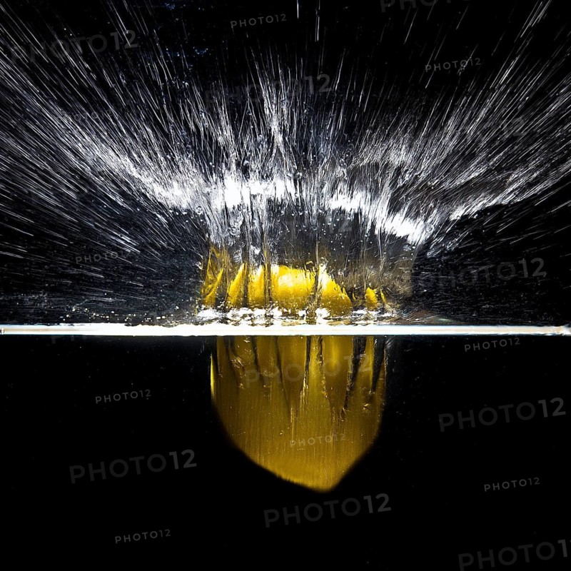 A fresh yellow lemon (Citrus limonum) falls into the water, creating a splash and air bubbles, against a black background