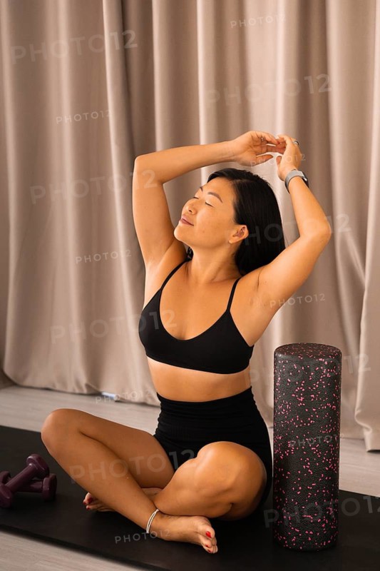Woman sitting cross-legged, stretching with foam roller, exuding calm and focus
