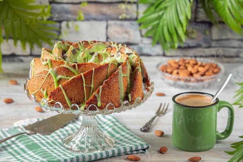 A cake with green icing next to a cup of coffee and almonds