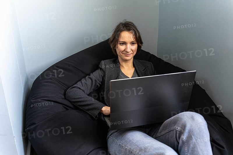Happy freelancer relaxing on bean bag with laptop in minimalist workspace
