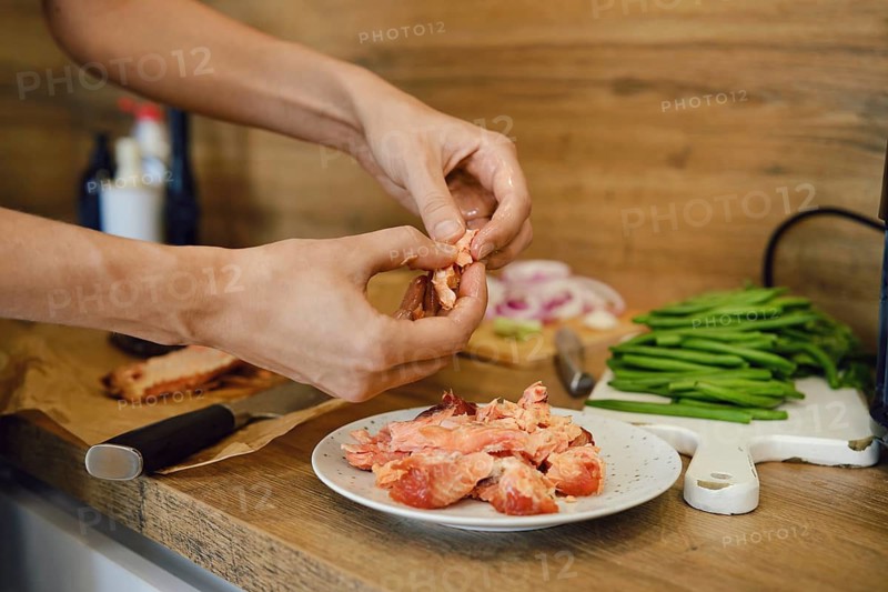 Person is removing bones from cooked salmon in kitchen. Several green beans and sliced onion are on a cutting board. A knife is placed next to the plate with salmon on a wooden surface
