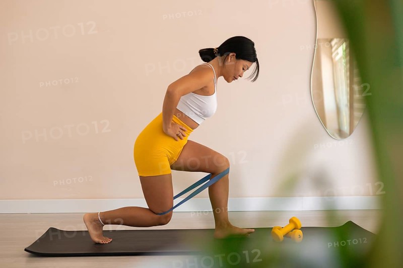 Determined woman lunging with resistance band in a bright room with plants