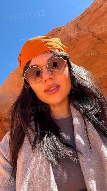 Young woman posing for a selfie during an adventure trip, wearing a bandana and sunglasses, exploring the unique sandstone rock formations and clear blue sky of antelope canyon