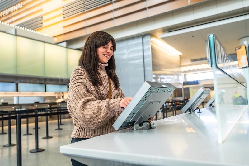 Woman smiles while using a digital self service check in kiosk at a modern airport terminal, processing flight details and boarding pass for travel convenience and efficiency