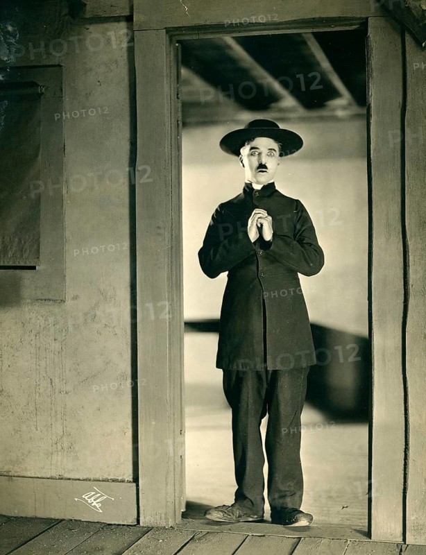 Charly Chaplin, The Tramp, silent film, 1915, disguised, priest, vagabond, comedian, USA, A man in an old-fashioned suit stands in a door with folded hands, James Abbe