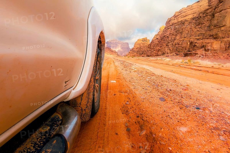 Close up 4wd vehicle driving across Wadi rum red sand track with desert mountains off road adventure travel. SUV driving through gravel dirt road hilly terrain landscape