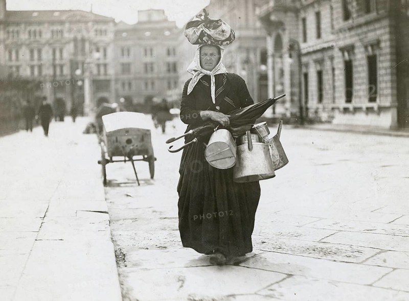 Munich, woman's work, outpatient business, selling umbrellas, watering cans, poverty, a woman carrying objects and tools on her head on a wide, empty street, Philipp Kester, around 1906