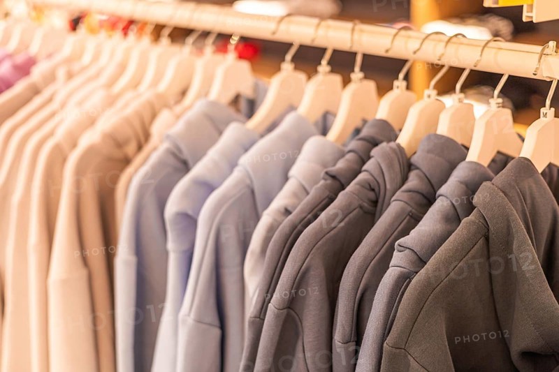 Hoodies displayed on hangers in a retail store. Various colors include gray, blue, and beige. The setting is bright and inviting, showcasing casual fashion