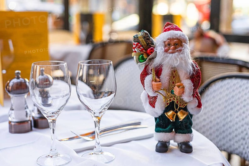A festive table setting with two wine glasses and a decorative Santa Claus figurine. The scene captures the spirit of Christmas and New Year celebrations