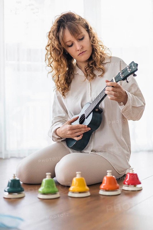 A woman in white focused on playing a ukulele with colorful bells