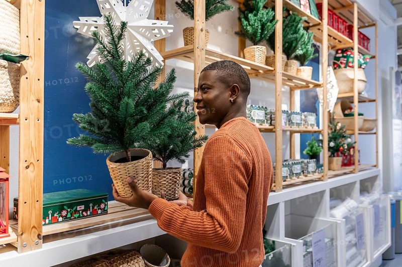 A smiling African American with a Christmas tree in his hands in store.