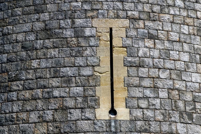 A tall narrow archery window is set into the coursed stonework of a curved tower at Windsor Castle, an opening originally designed to let defenders shoot arrows while sheltering behind the thickness of the medieval wall, Windsor, England, United Kingdom