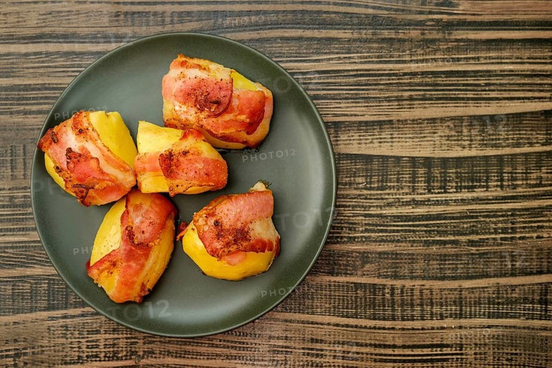 Top view of plate with roasted potatoes wrapped in bacon on wooden table