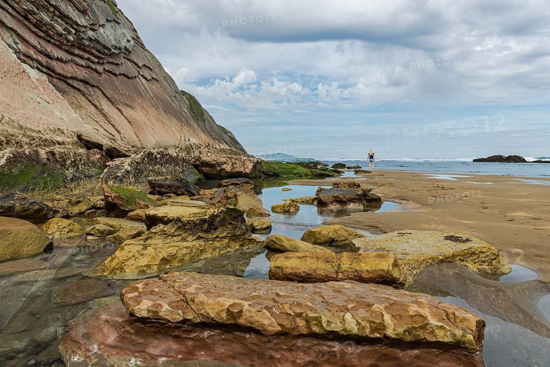 Woman on the horizon on prominent rock cliffs as a geological formation made of rock layers, Flysch on Itzurun Beach in Zumaia, Spain