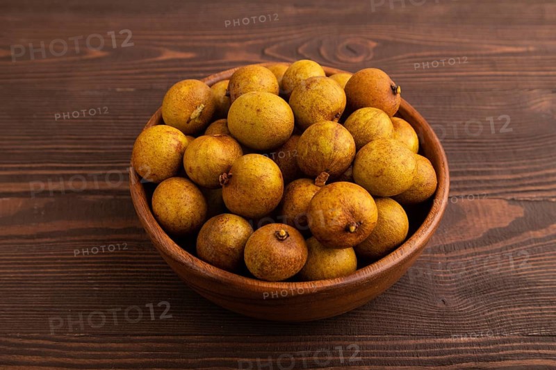 Ripe Longan in wooden bowl on brown wooden background, side view, close up, minimalism