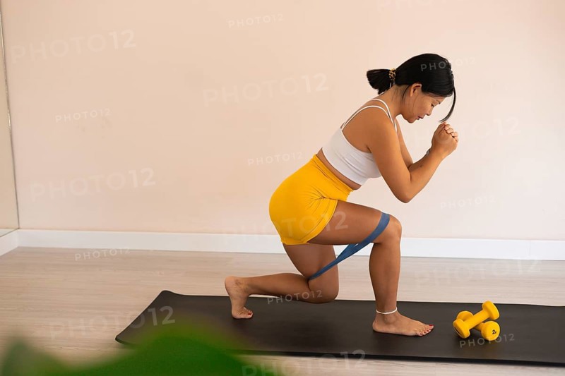 Focused woman performing lunges with resistance band on a mat in a home gym