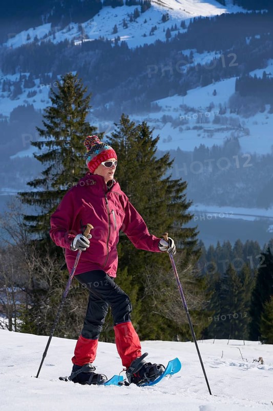 Sportive senior woman hiking with snow shoes in the snowy Allgaeu Alps above Lake Alosee, Immenstadt, Bavria, Germany