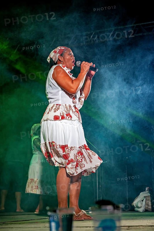 A woman sings on a stage in smoke surrounded by green light and floral patterns, a band plays and dances at a festival in Petrolina in Brazil
