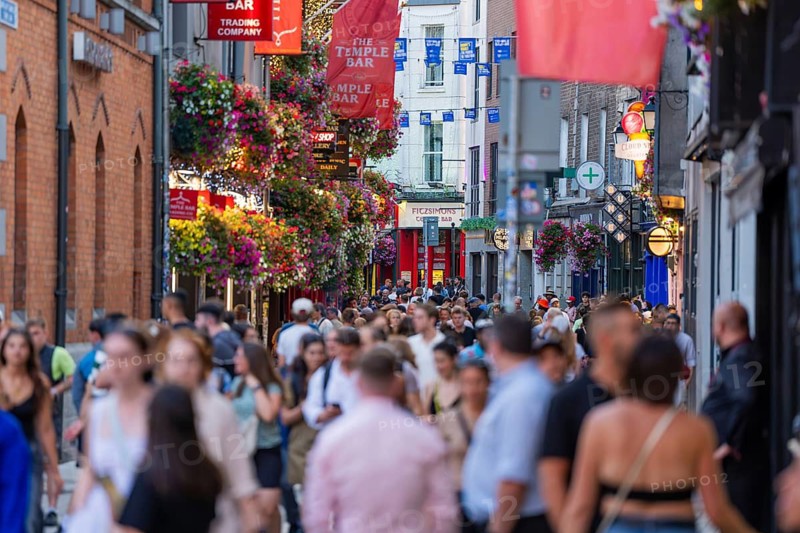A dense crowd on a busy street with hanging baskets and flags, Dublin, Ireland
