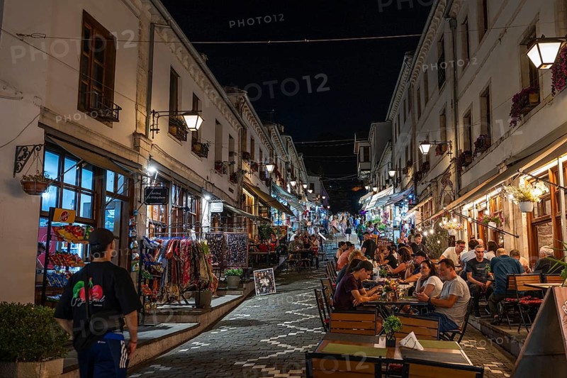 GJIROKASTER, ALBANIA - JUNE 30, 2026: People dining at outdoor restaurant tables along a cobblestone street at night in the old bazaar