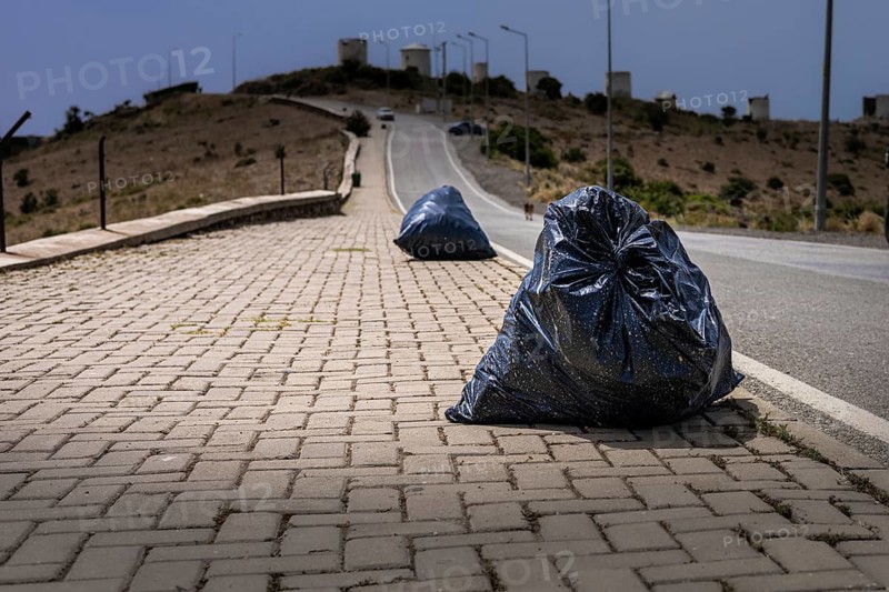 Two black garbage bags on a paved road in a barren landscape. The scene highlights environmental issues and waste management challenges
