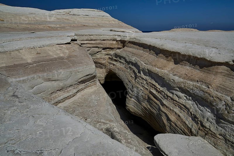 Rocky crevice and cave in dry rocky environment under clear sky, white volcanic rock, bizarre white rocks in the sea, Little Sarakiniko, Kioni Beach, Kioni, Kimolos Island, Cyclades, Greek Islands, Greece
