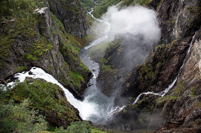 A dramatic waterfall tumbles through a steep, misty gorge amid green vegetation, The Vøringfossen Waterfall on the western edge of Hardangervidda, Norway, Scandinavia