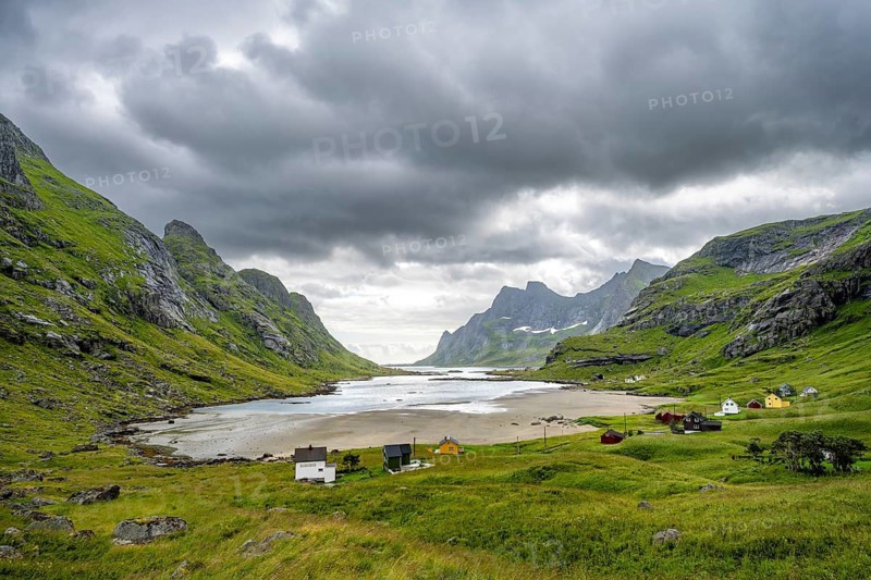 Houses on Bunesfjorden fjord, green mountain landscape and dark clouds, Lofoten, Norway