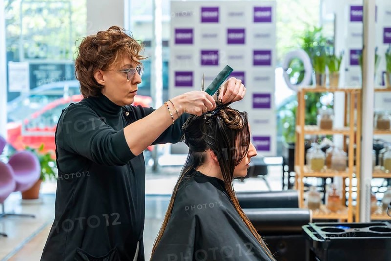 Hairdresser performing a haircut preparation for a female customer in a modern salon, sectioning wet hair with a comb and clips before styling, creating a clean look