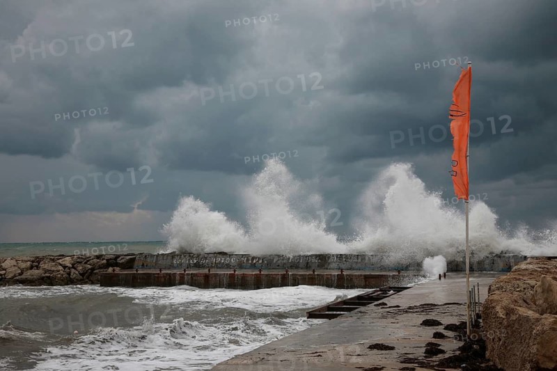 Stormy sea with high waves, grey sky and an orange flag in the foreground, Cyprus