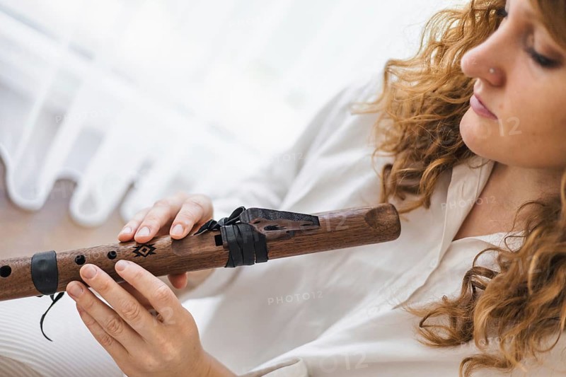 A focused woman examines a wooden flute, highlighting the crafted details