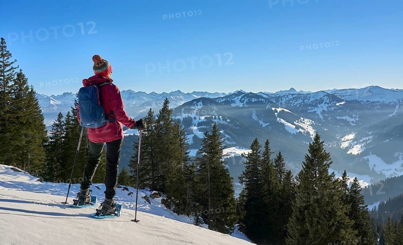Nice and active senior woman snowshoeing in in the snow covered Allgaue alps above the valley of river Iller, Immenstadt, Bavaria, Germany