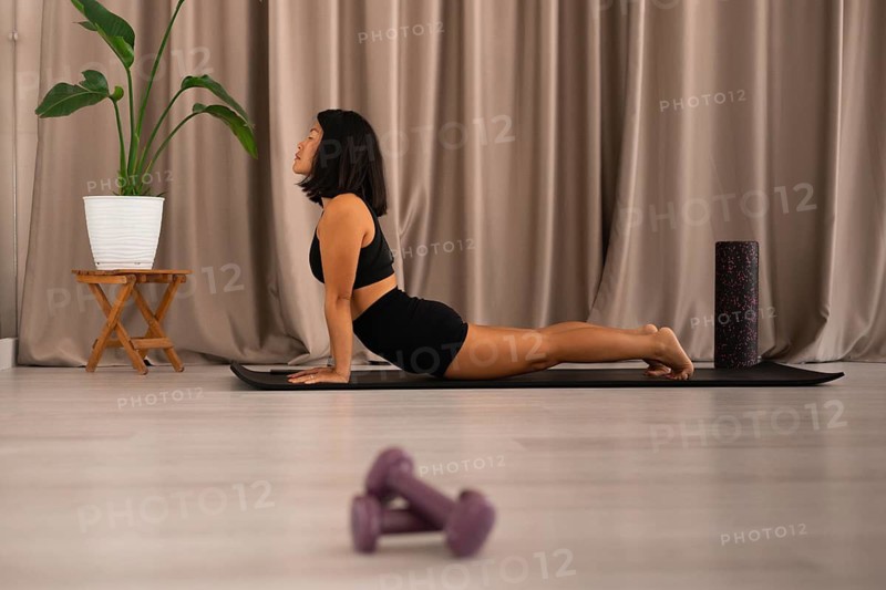 Woman in yoga stretch, mat on the floor, dumbbells and plant enhancing the relaxed atmosphere