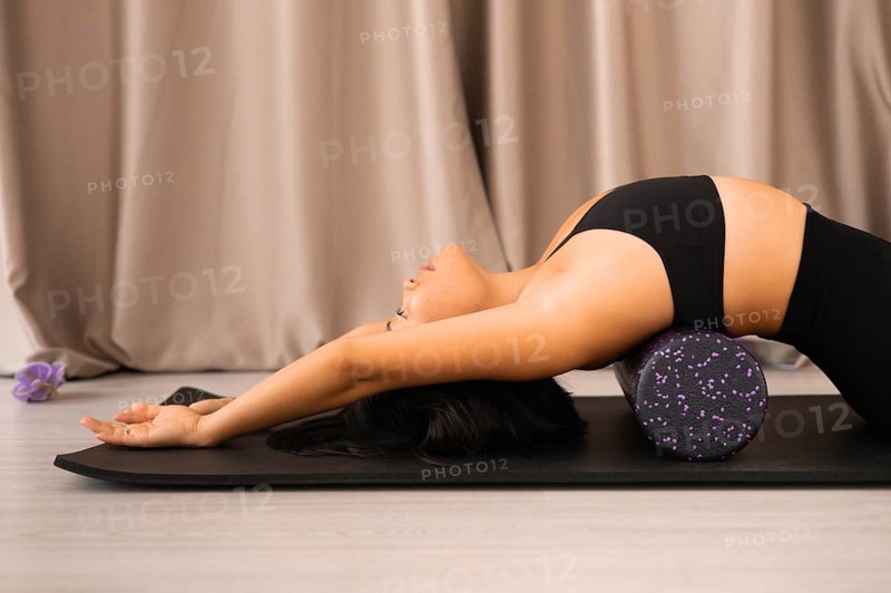Side view of a woman lying back on a foam roller on a yoga mat with a calm ambiance