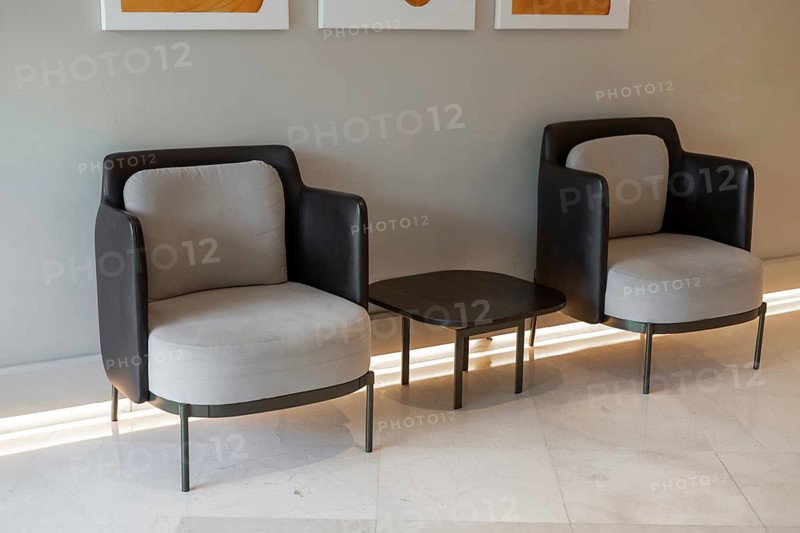 Two modern armchairs with a small table in between, set against a neutral wall. The chairs have a sleek design with a mix of black and gray upholstery