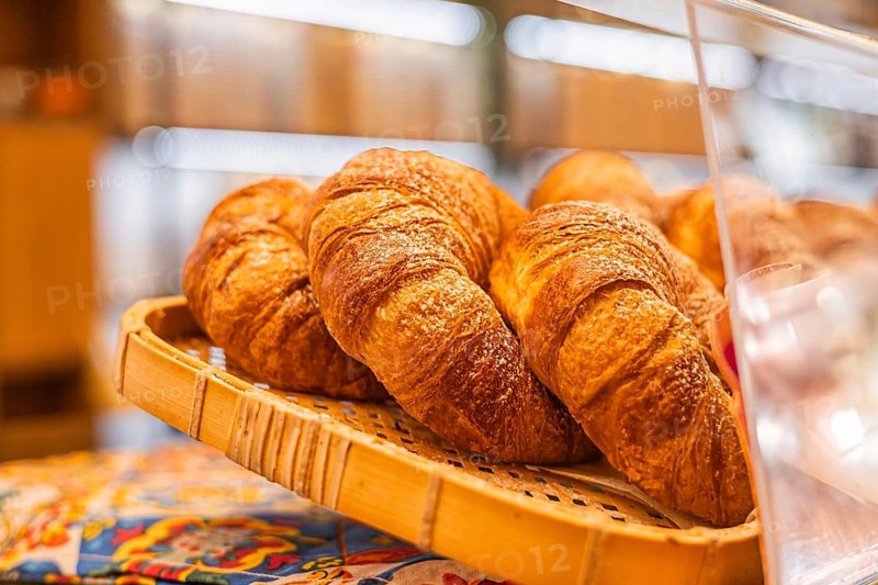 Freshly baked croissants arranged in a wicker basket. The croissants are golden brown and flaky, showcasing a delicious pastry treat
