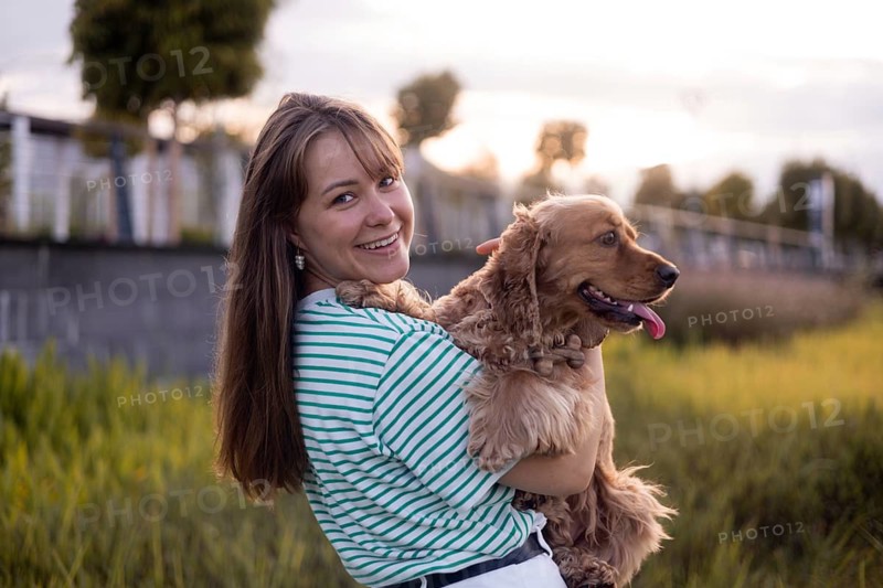 A woman holds her dog close as they enjoy a calm evening in a lush park