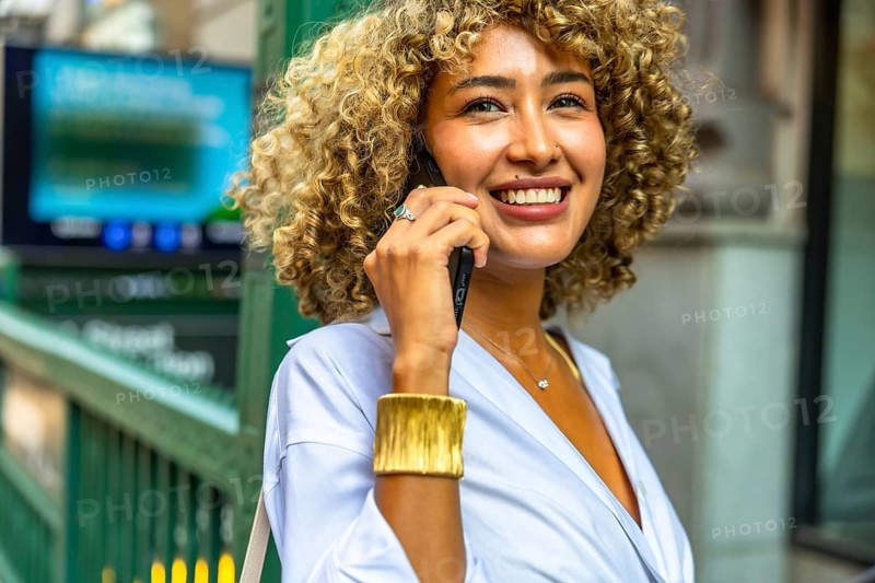 Smiling young woman communicating on her smartphone while standing near a subway entrance in manhattan, embracing the vibrant energy and modern lifestyle of the urban environment