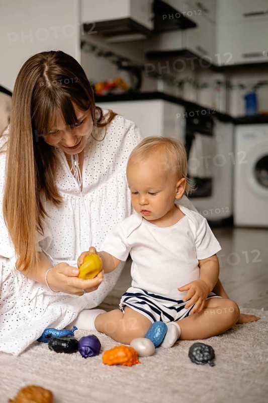 Mother showing a yellow toy to her baby on the floor
