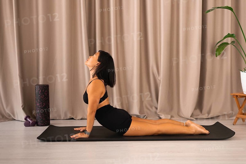 Woman performing upward dog pose on a mat in front of curtains