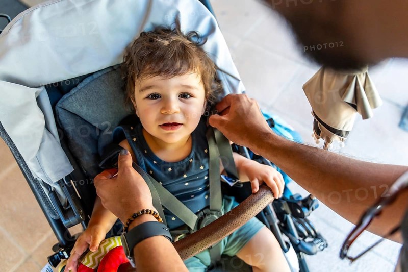Father's hands securing the safety harness on his young son sitting in a stroller, showing care, protection, and parental responsibility during family outings