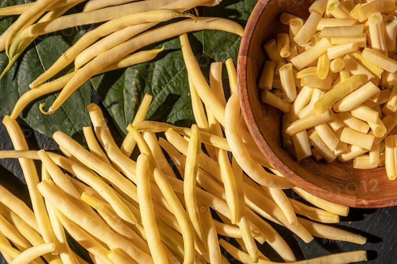 Sliced yellow beans in a bowl next to other beans and leaves