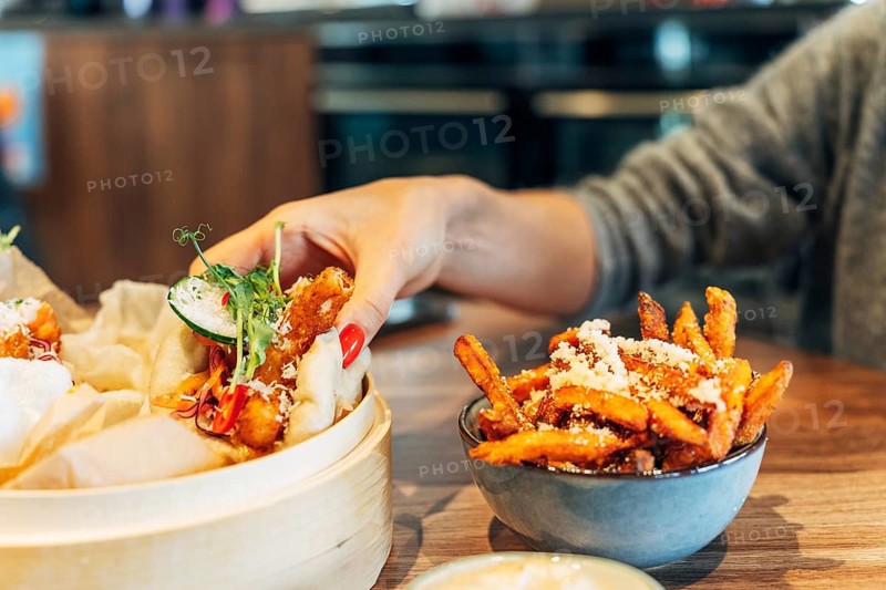 Woman picking up a gourmet bao bun from a steaming bamboo basket in a stylish restaurant